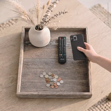an ottoman tray on top of a coffee table with remote and vase